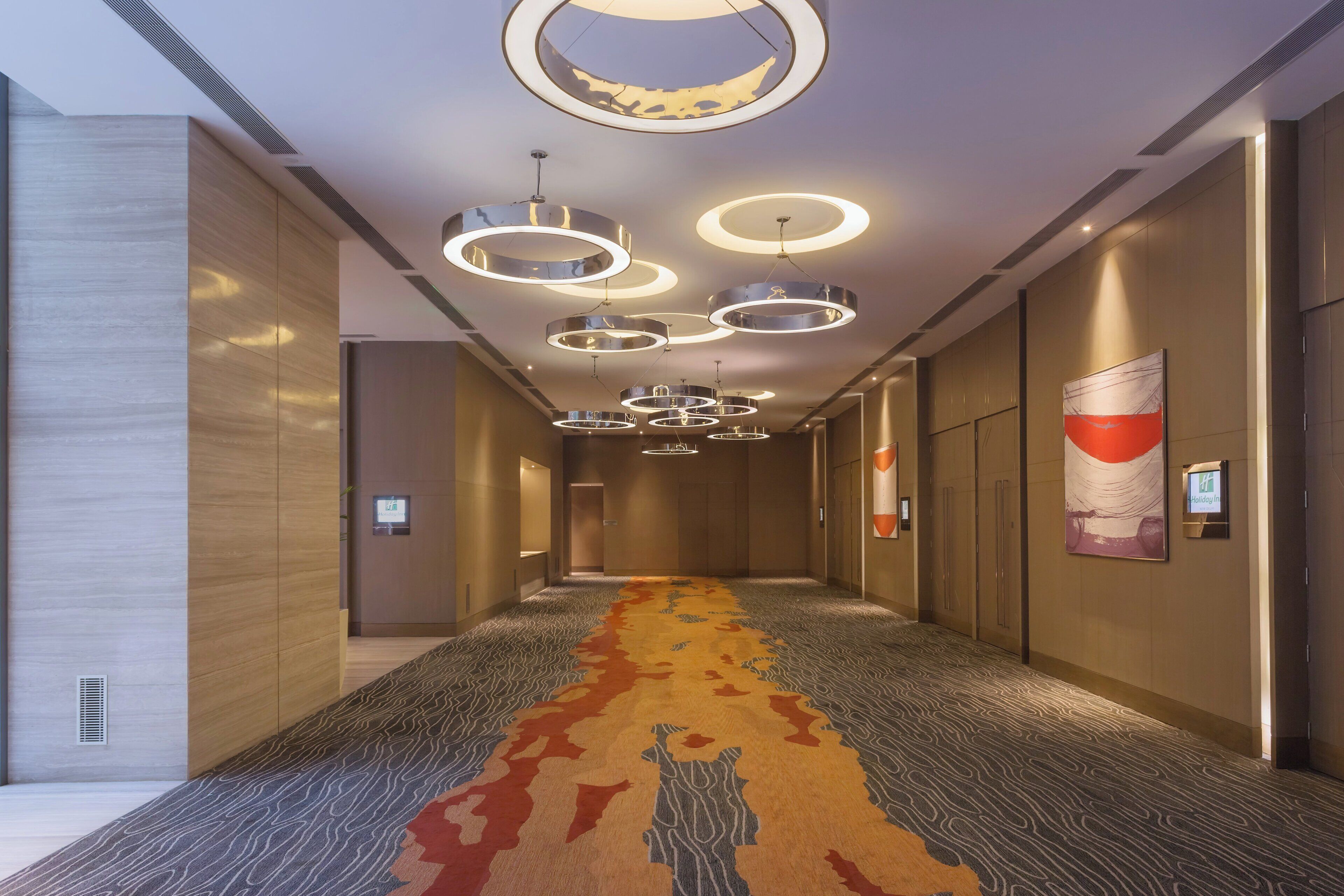 A hotel corridor with modern lighting fixtures, a patterned carpet, and a Holiday Inn sign.