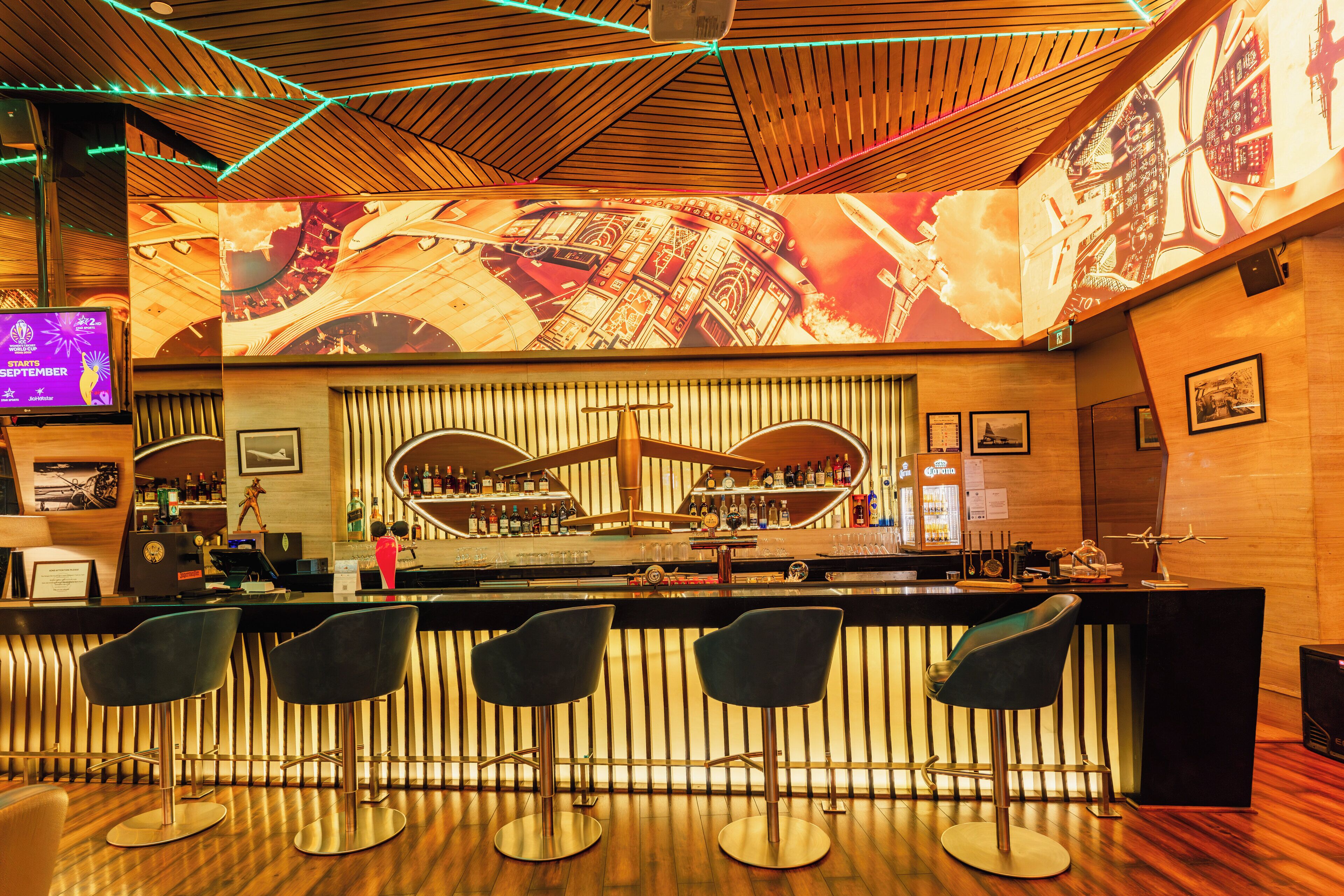 A bar area with a wooden ceiling, a large illuminated map, and a bar counter with stools.