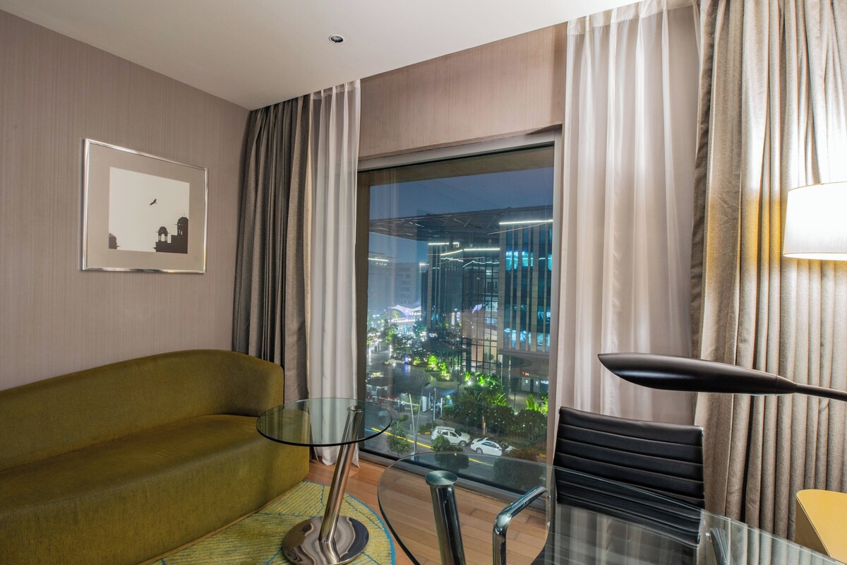 Een moderne hotelkamer met een glazen tafel, een bank en uitzicht op een stadsbeeld 's nachts.