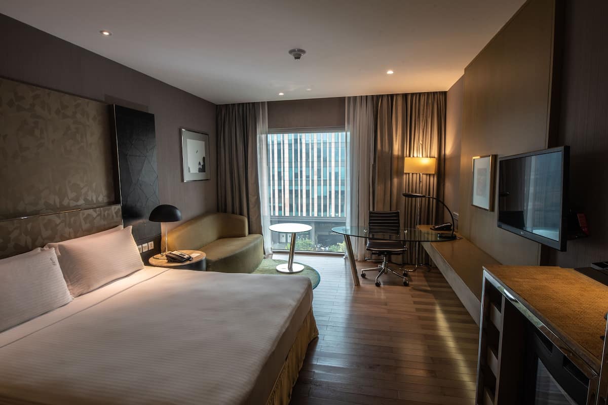 A hotel room with a large bed, a desk, a chair, a small table, a TV, and a window with curtains.