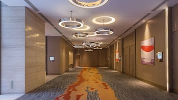 Hotel corridor with carpeted floor and wooden paneling, featuring pendant lights and doors leading to guest rooms.