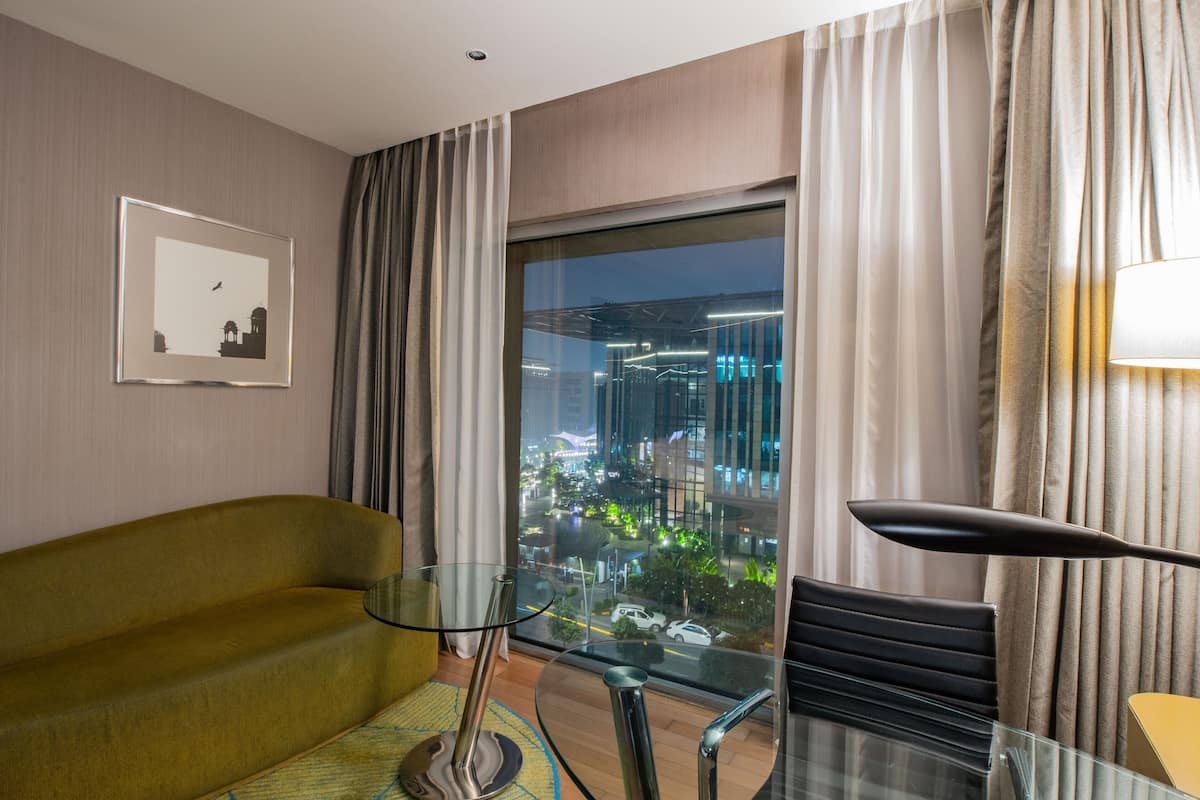 A modern hotel room with a glass table, a sofa, and a view of a cityscape at night.