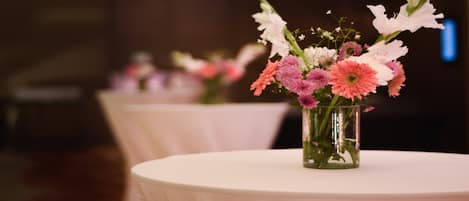 Una mesa con un florero de vidrio transparente que contiene flores rosas y blancas, sobre un mantel blanco.