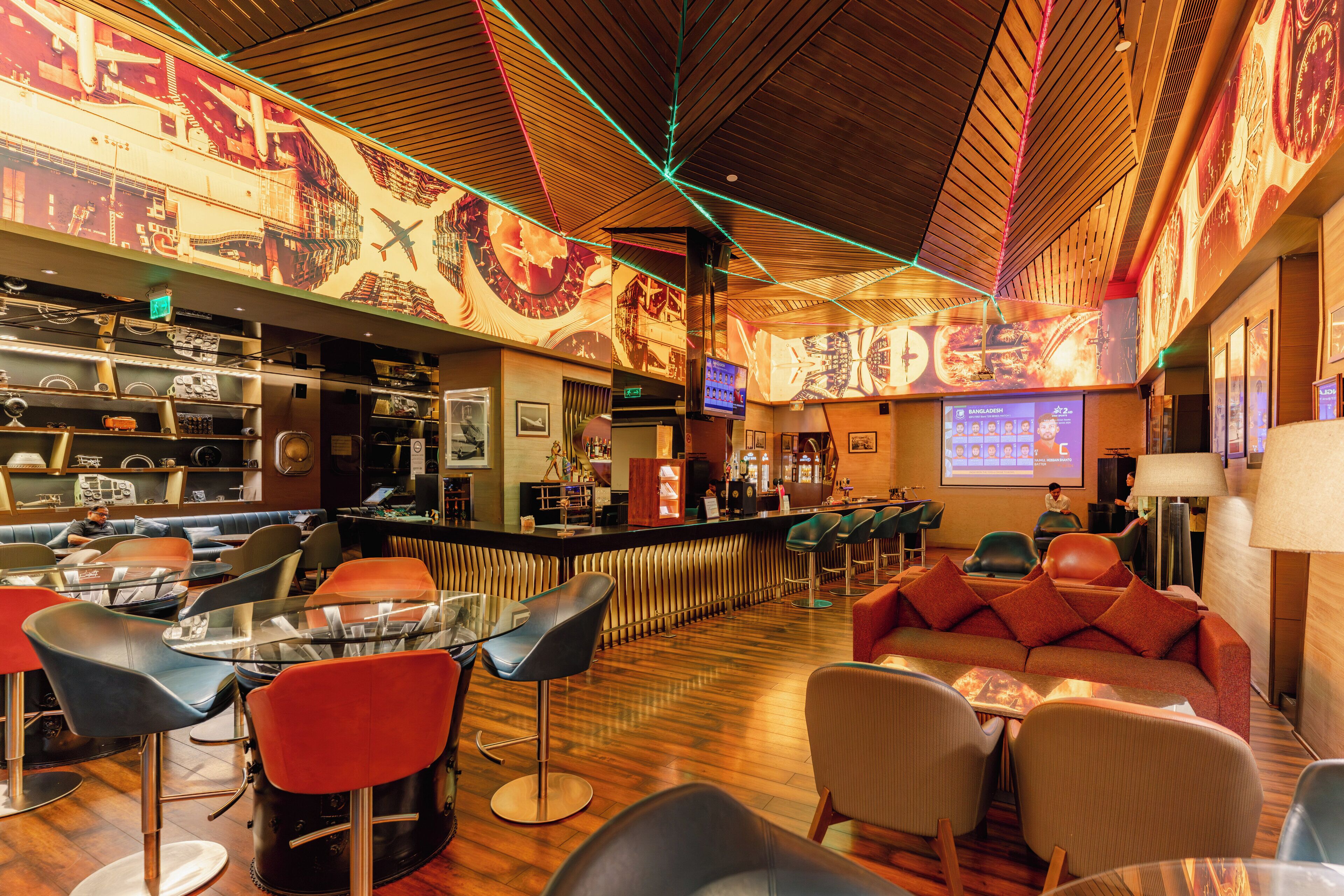 A bar area with a wooden ceiling, bar counter, and seating including bar stools and a sofa.