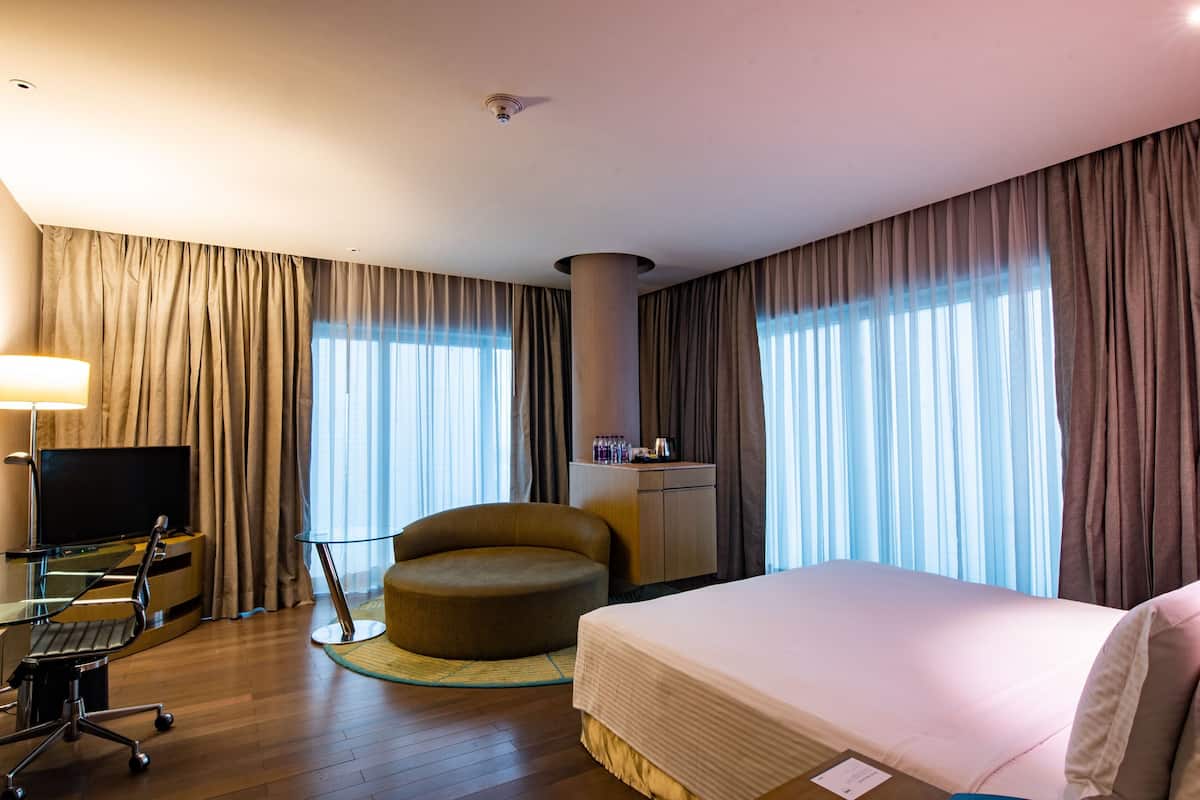 A hotel room with a bed, a desk with a computer, a chair, a TV, and a minibar.
