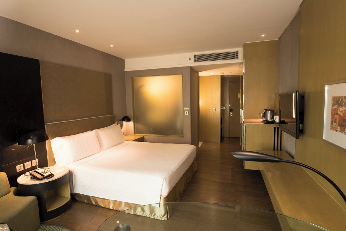 Een moderne hotelkamer met een groot bed, nachtkastje met een lamp, een flatscreen-tv aan de muur en een klein kitchenette-gedeelte.