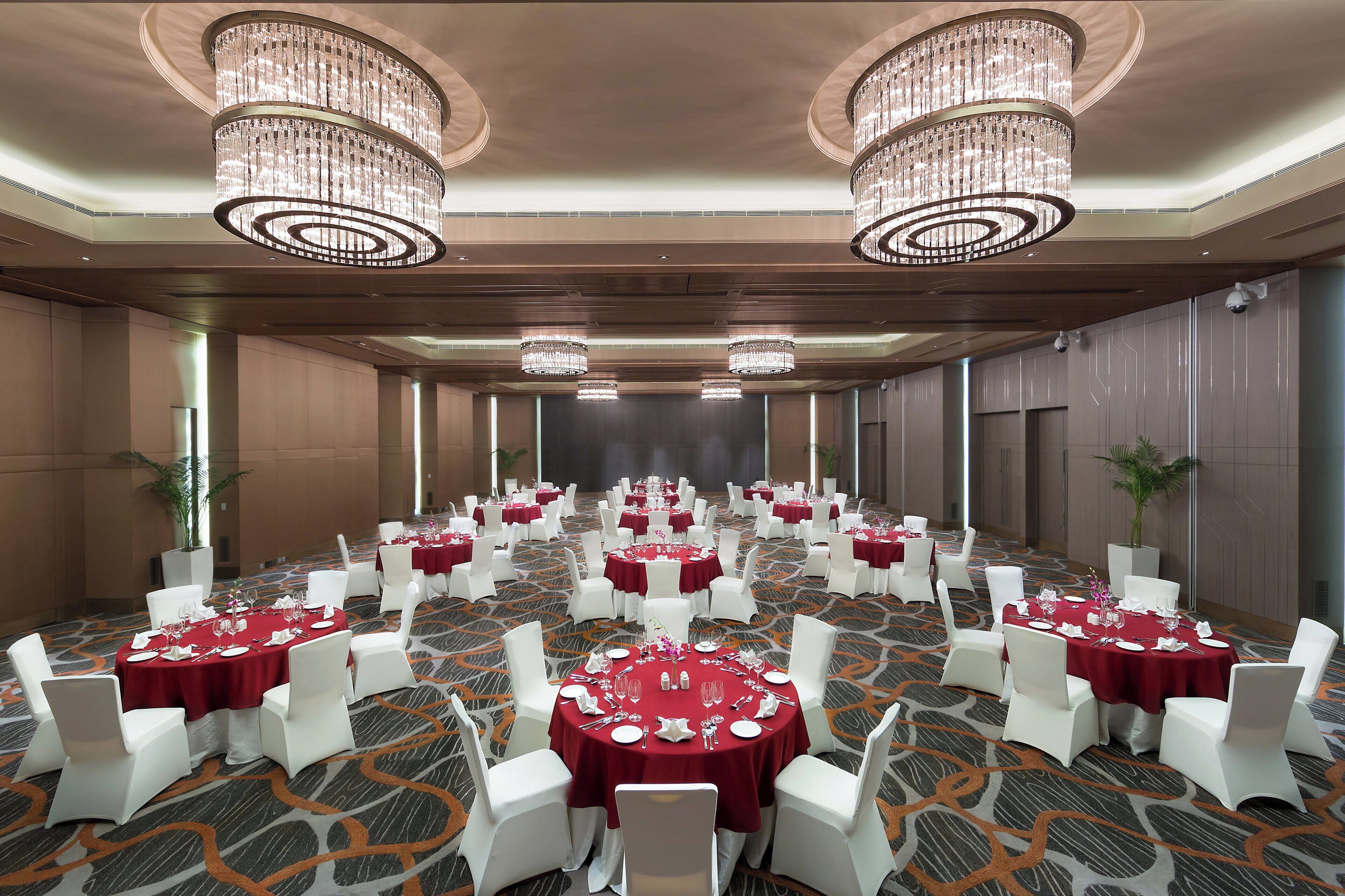 A banquet hall with round tables, white chairs, and chandeliers.