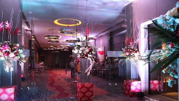 Un hall d’hôtel moderne, avec un tapis rouge, des cloisons en verre et des compositions florales décoratives.