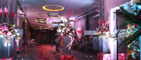 A modern hotel lobby with a red carpet, glass partitions, and decorative floral arrangements.