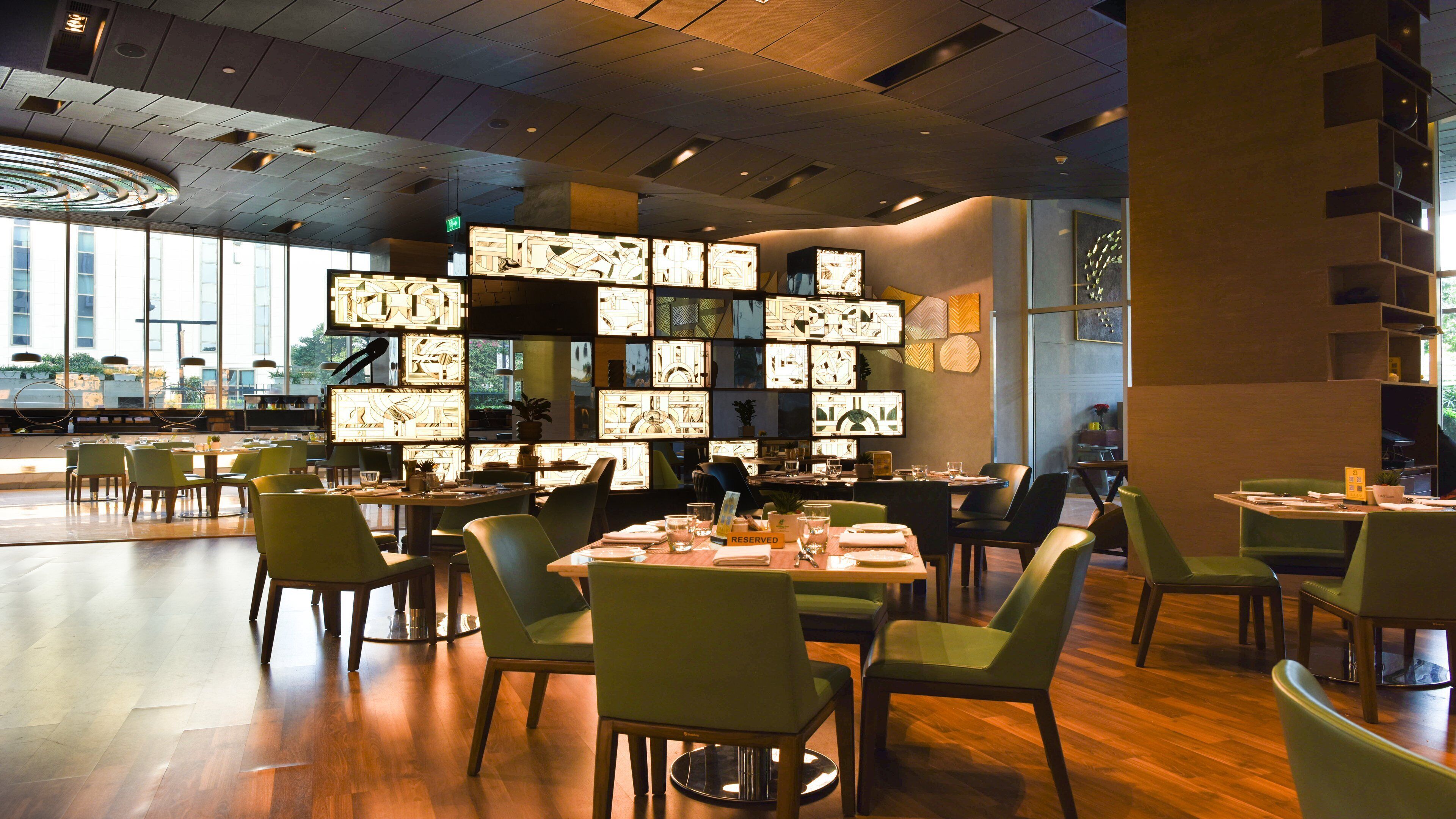 Een restaurant met meerdere tafels en stoelen, een modern plafondontwerp en grote ramen die voor natuurlijk licht zorgen.