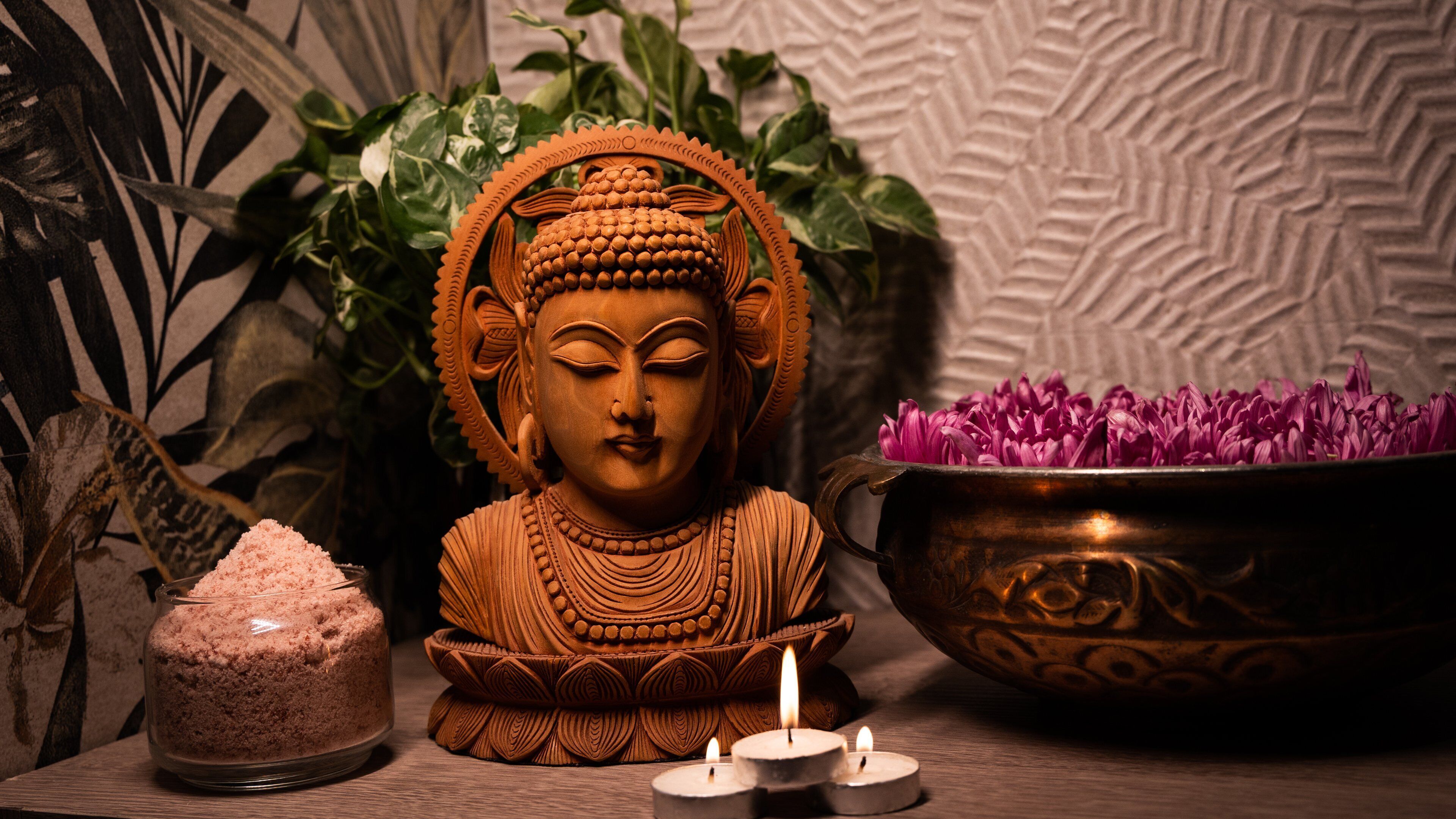 A statue of a seated figure with a bowl of purple flowers and two lit candles on a table.