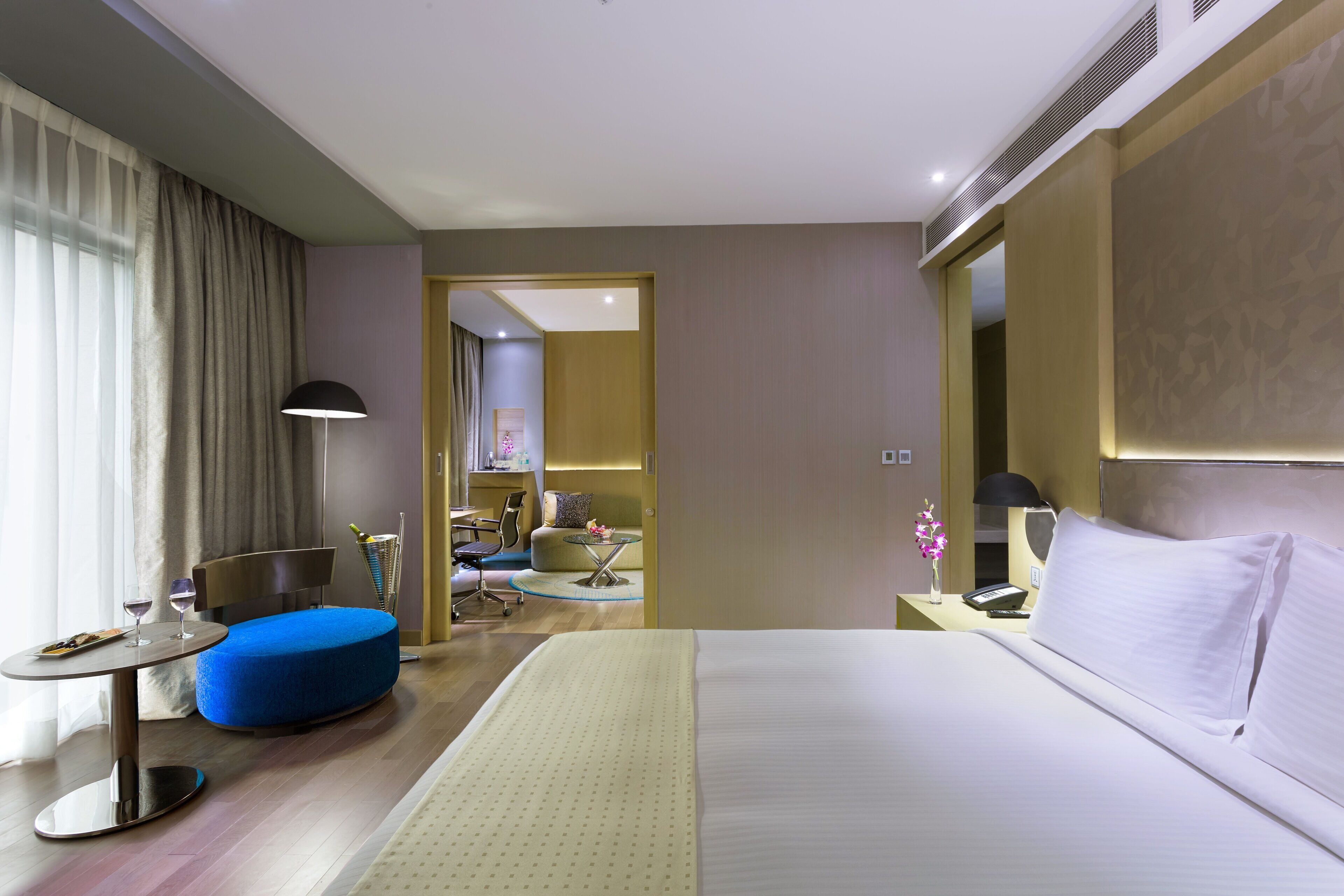 A hotel room with a bed, a desk, a chair, a small table, and a blue ottoman.