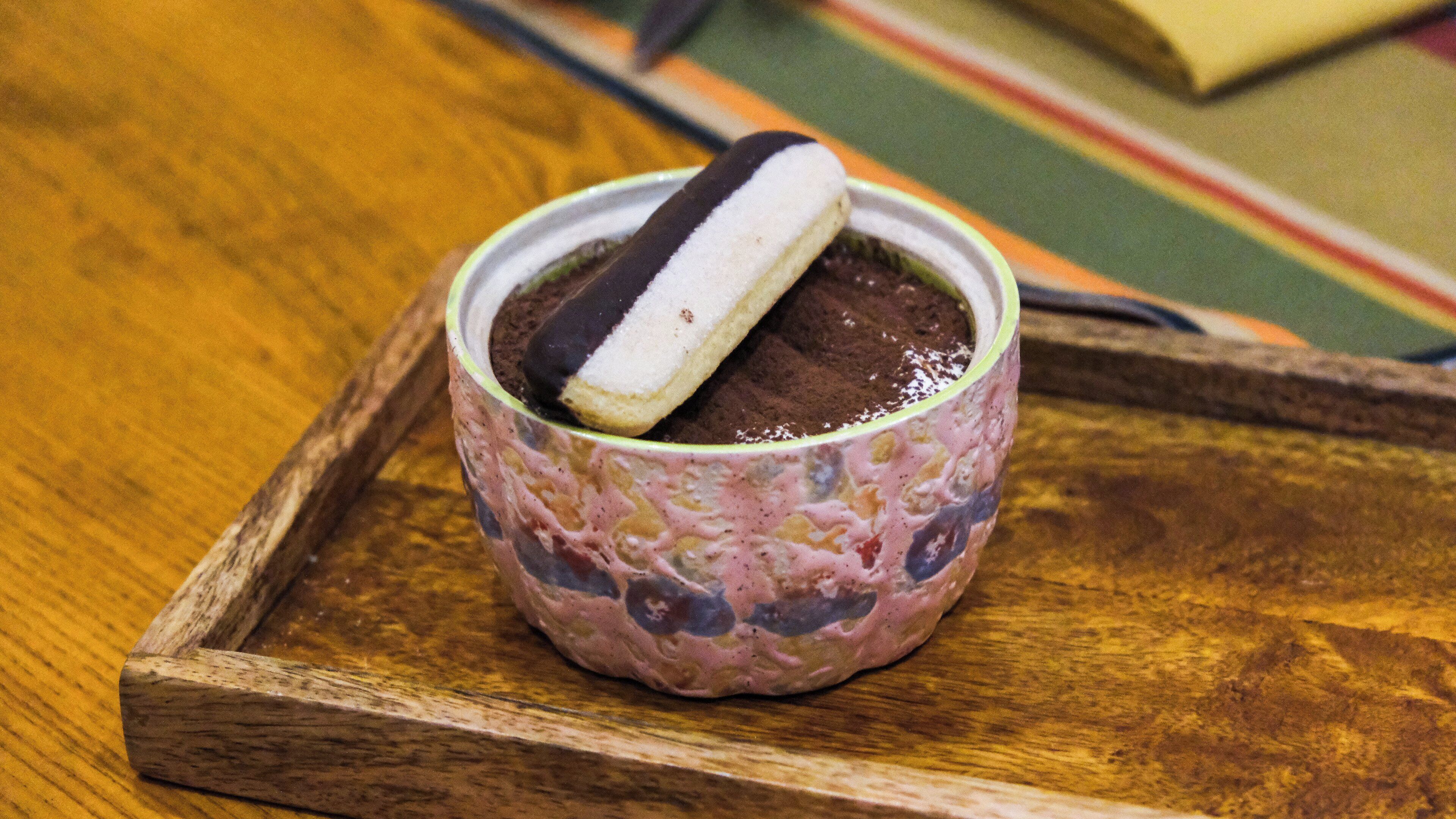 A cup of dessert with a chocolate-covered biscuit on a wooden tray.