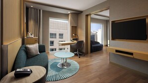 Een moderne hotelkamer met een bank, een klein rond tafeltje, een bureau, een stoel en een aan de muur bevestigde televisie.