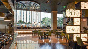 Een modern restaurant met een glazen wand, groene stoelen en uitzicht op gebouwen.