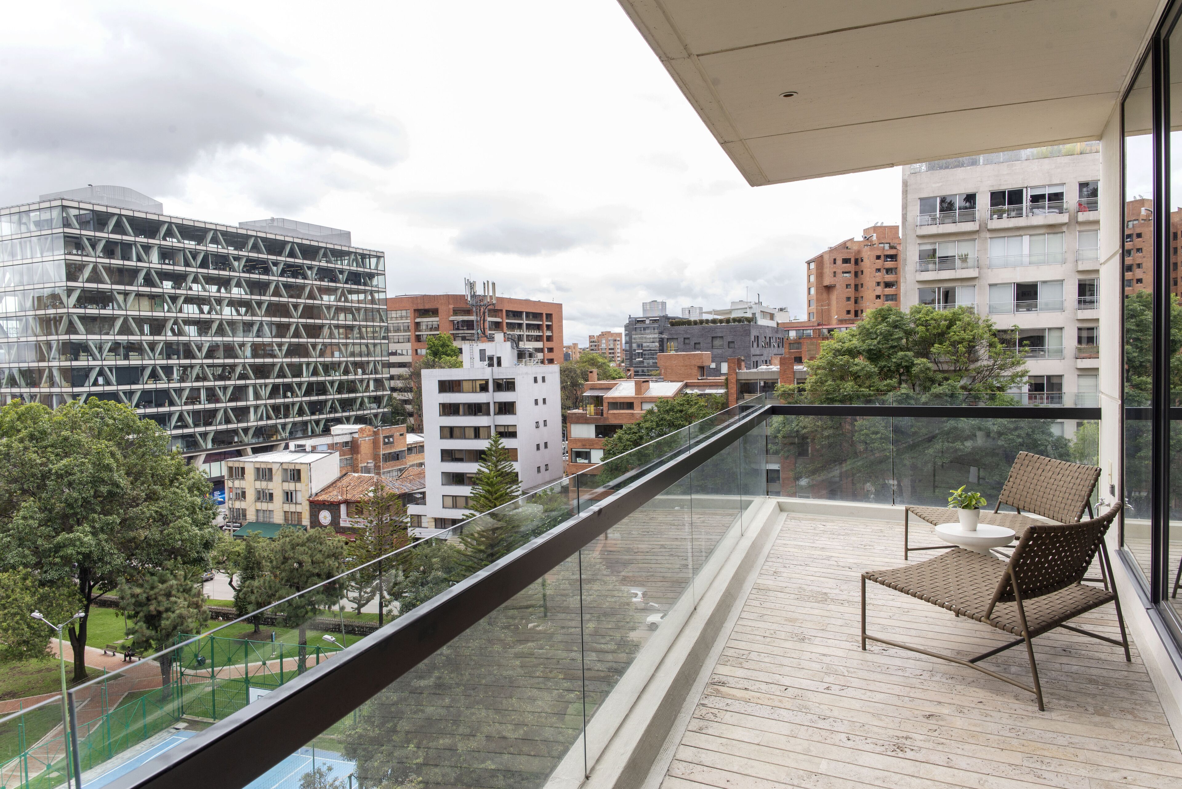 A balcony with a glass railing, a wooden deck, and two wicker chairs.