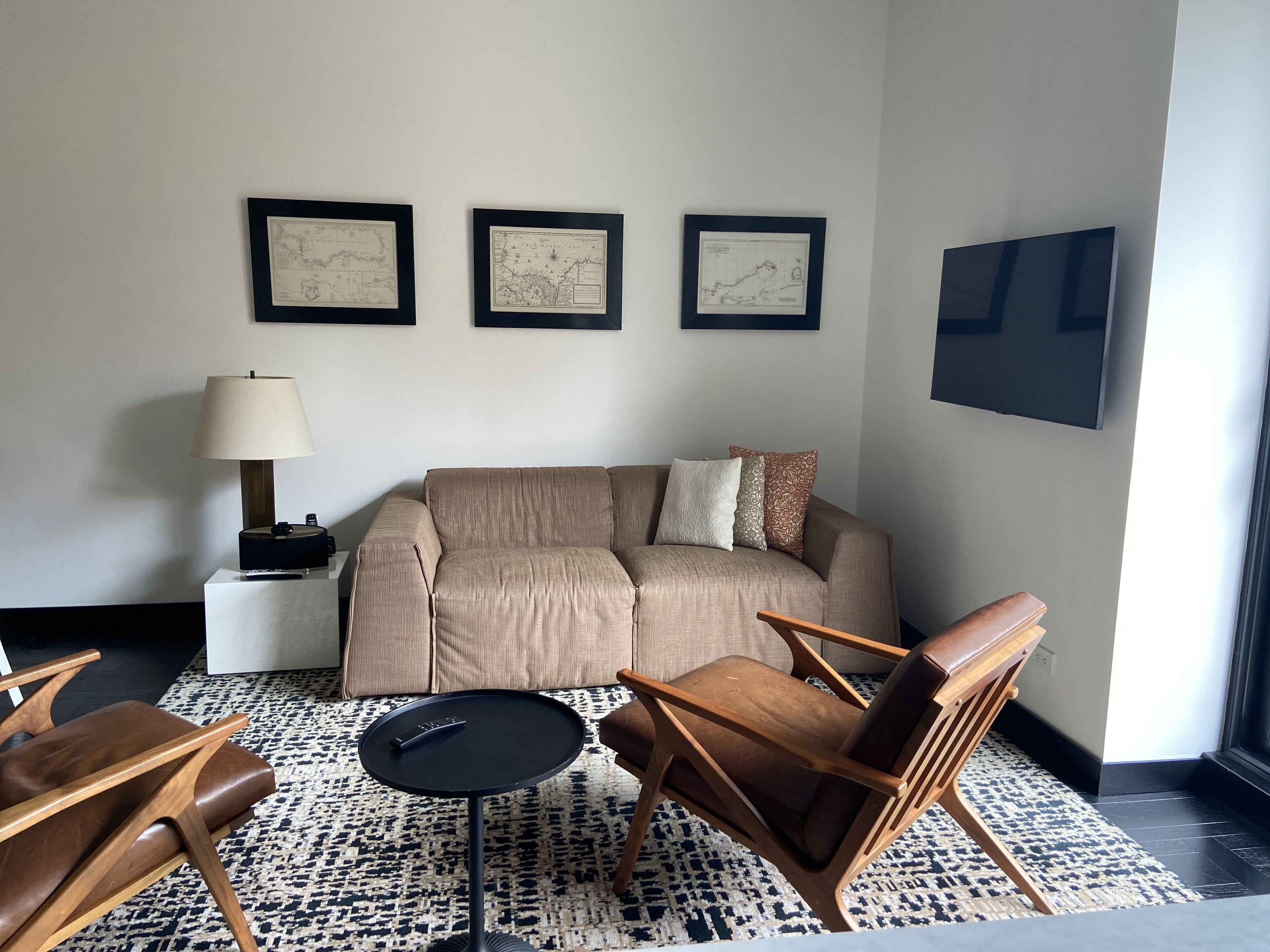 Una sala moderna con un sofá, dos sillones, una mesa de centro, una lámpara y tres mapas enmarcados en la pared.