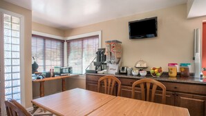 A kitchen with a wooden table, chairs, a coffee maker, a microwave, and a TV mounted on the wall. - The Hillside Hotel (Knoxville)
