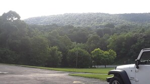 A white off-road vehicle parked in a parking lot with a backdrop of a forested hill. - The Hillside Hotel (Knoxville)