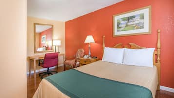 A hotel room with a bed, desk, chair, and a painting on the wall.
