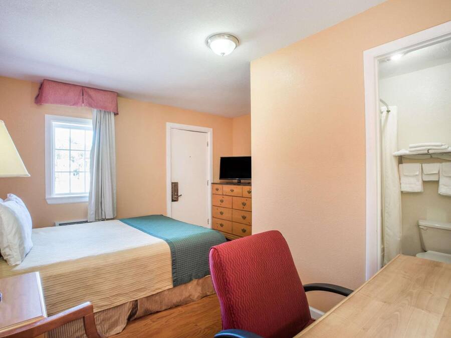 A small hotel room with two beds, a desk, a chair, a television, and a bathroom with towels.