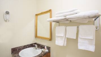 A bathroom with a marble sink, a gold-framed mirror, and a towel rack with folded towels.