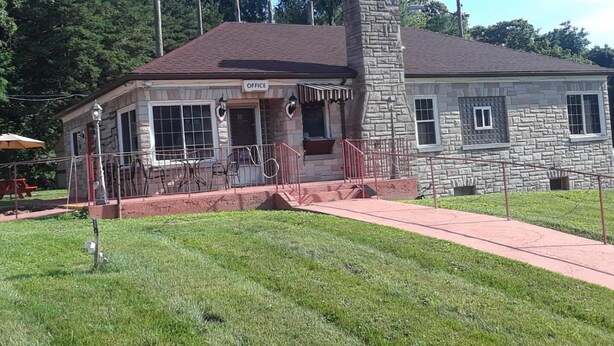 A stone building with a chimney, a porch with outdoor seating, and a sign that reads "OFFICE". - The Hillside Hotel (Knoxville)