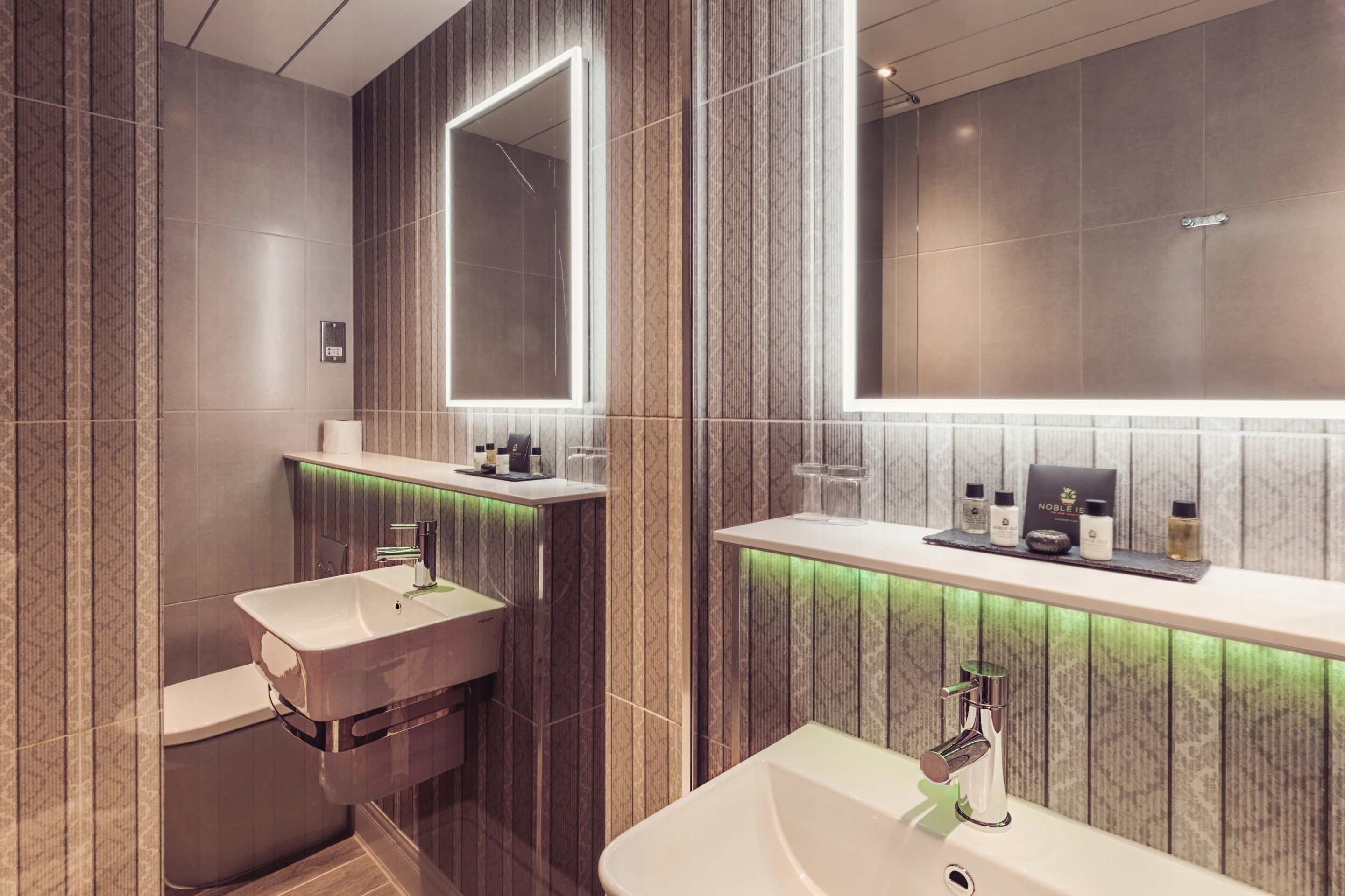 A modern bathroom with two sinks, a mirror, and a vanity with a green-lit vanity light.