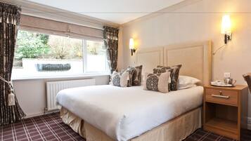 A neatly made bed with patterned pillows, a bedside table with a lamp, and a view of greenery through the window.