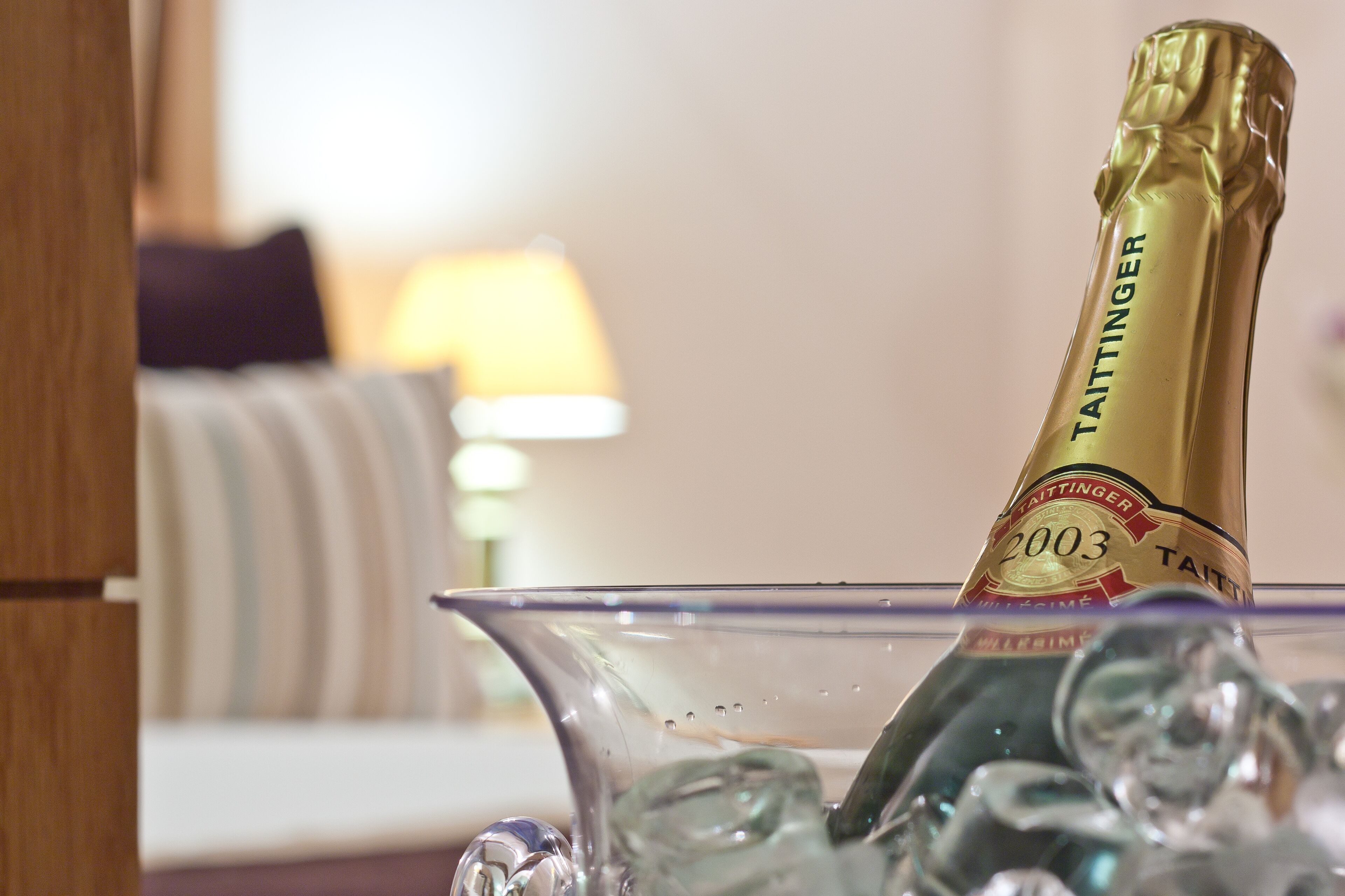 A champagne bottle labeled 'Taittinger 2003' in a glass bowl with ice cubes.