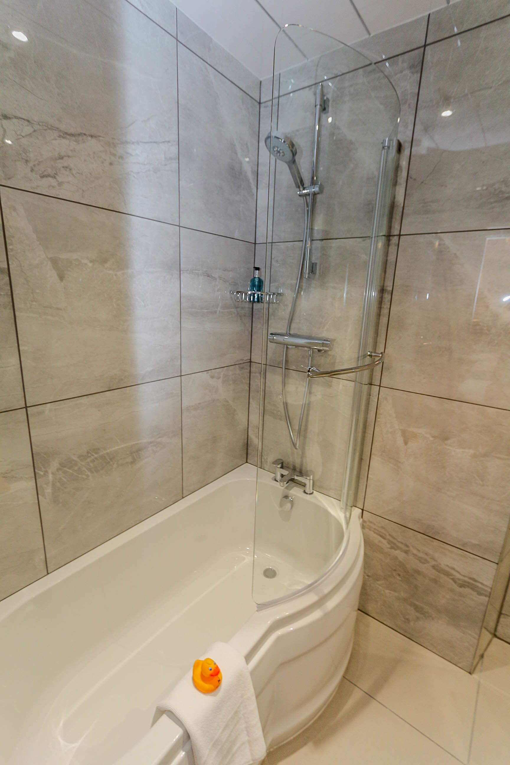 A modern bathroom with a glass-enclosed shower, a white bathtub, and beige tiled walls.