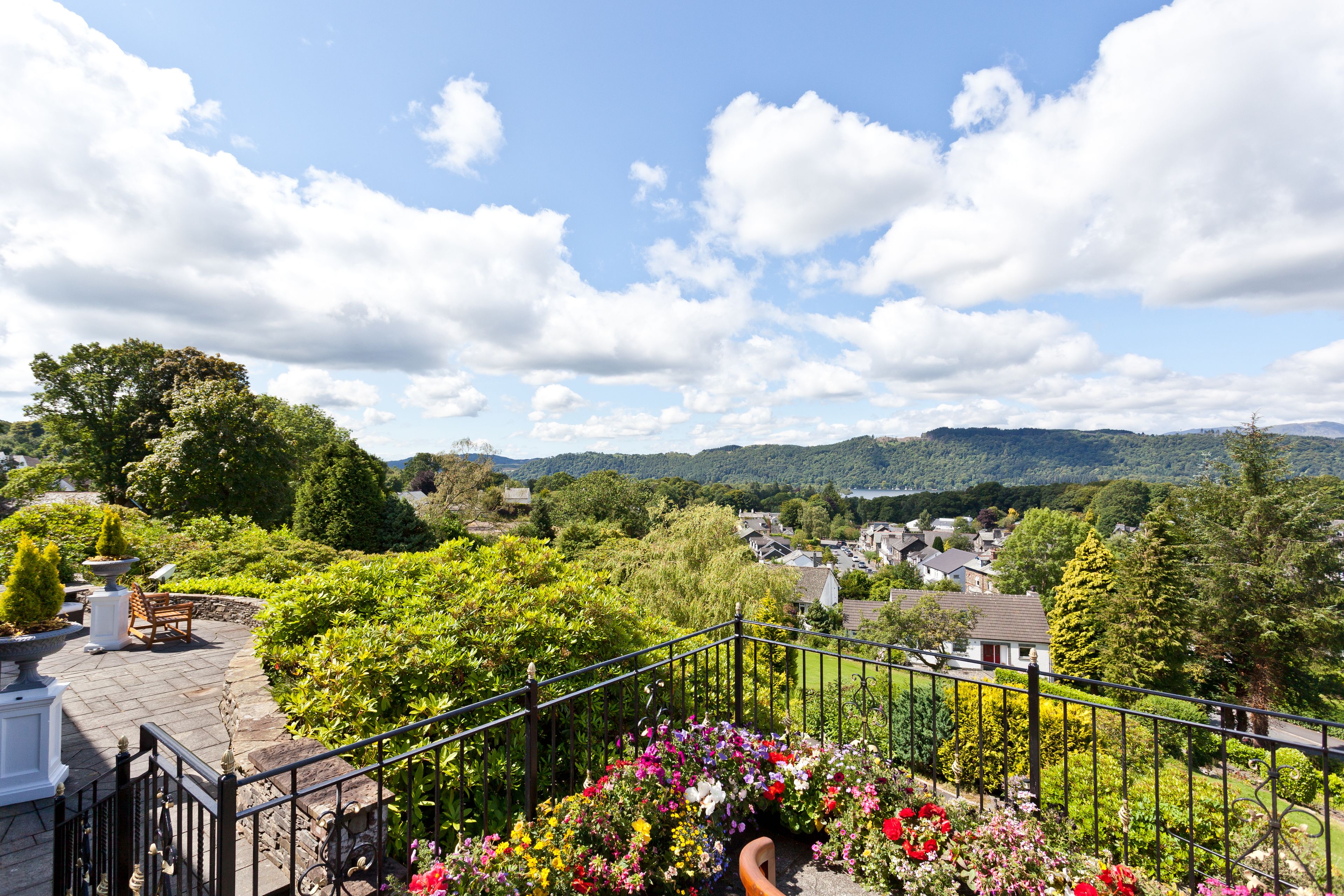 A garden with a stone bench, a metal railing, and a variety of flowers.