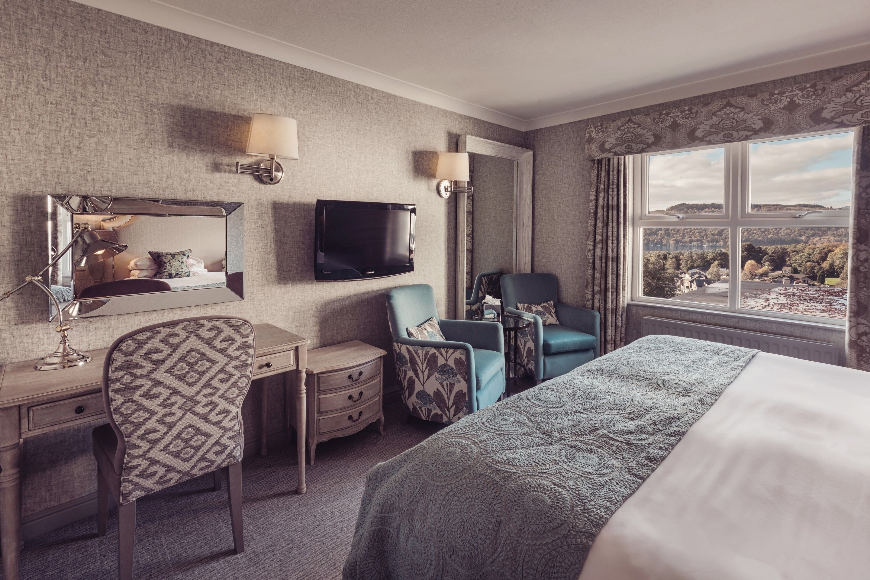 Hotelkamer met een groot bed, een bureau met spiegel, een televisie en uitzicht op het omliggende landschap.