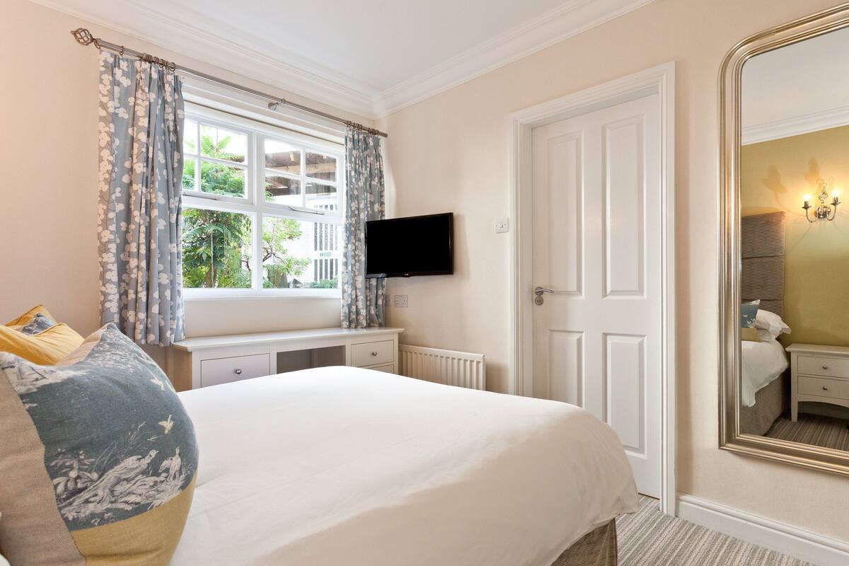 A bedroom with a large bed, a television mounted on the wall, a window with curtains, and a mirror on the wall.