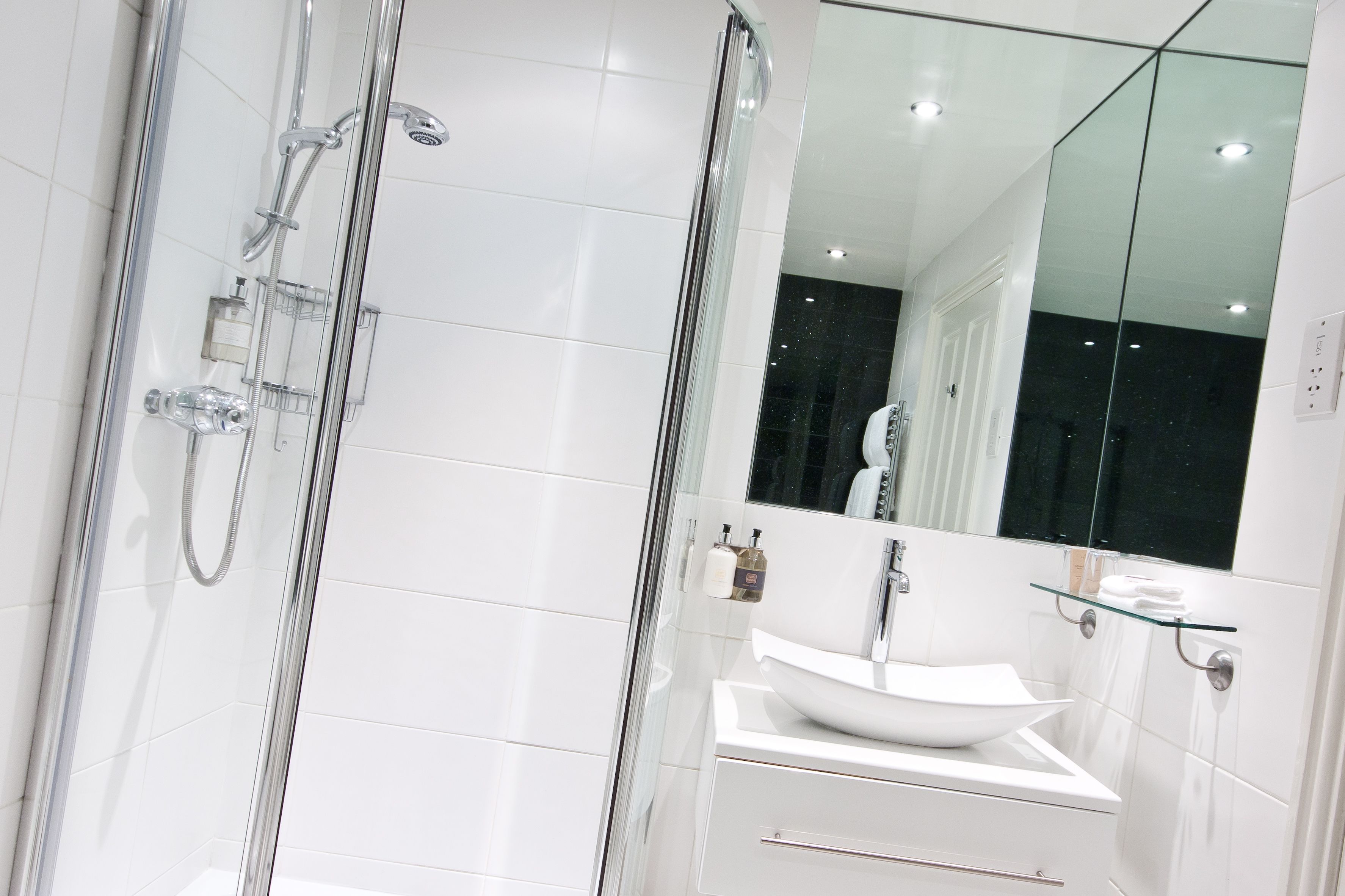 A modern bathroom with a glass-enclosed shower, a white sink, and a large mirror.