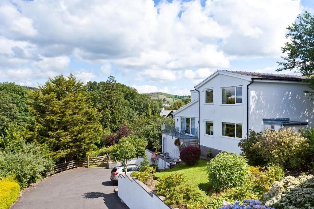 Une maison moderne à deux étages, avec une façade blanche, un porche à l’avant et une allée menant à une voiture garée.