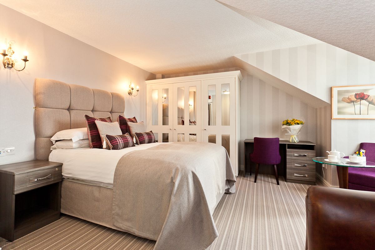 A hotel room with a large bed, a desk, a wardrobe, and a chair.