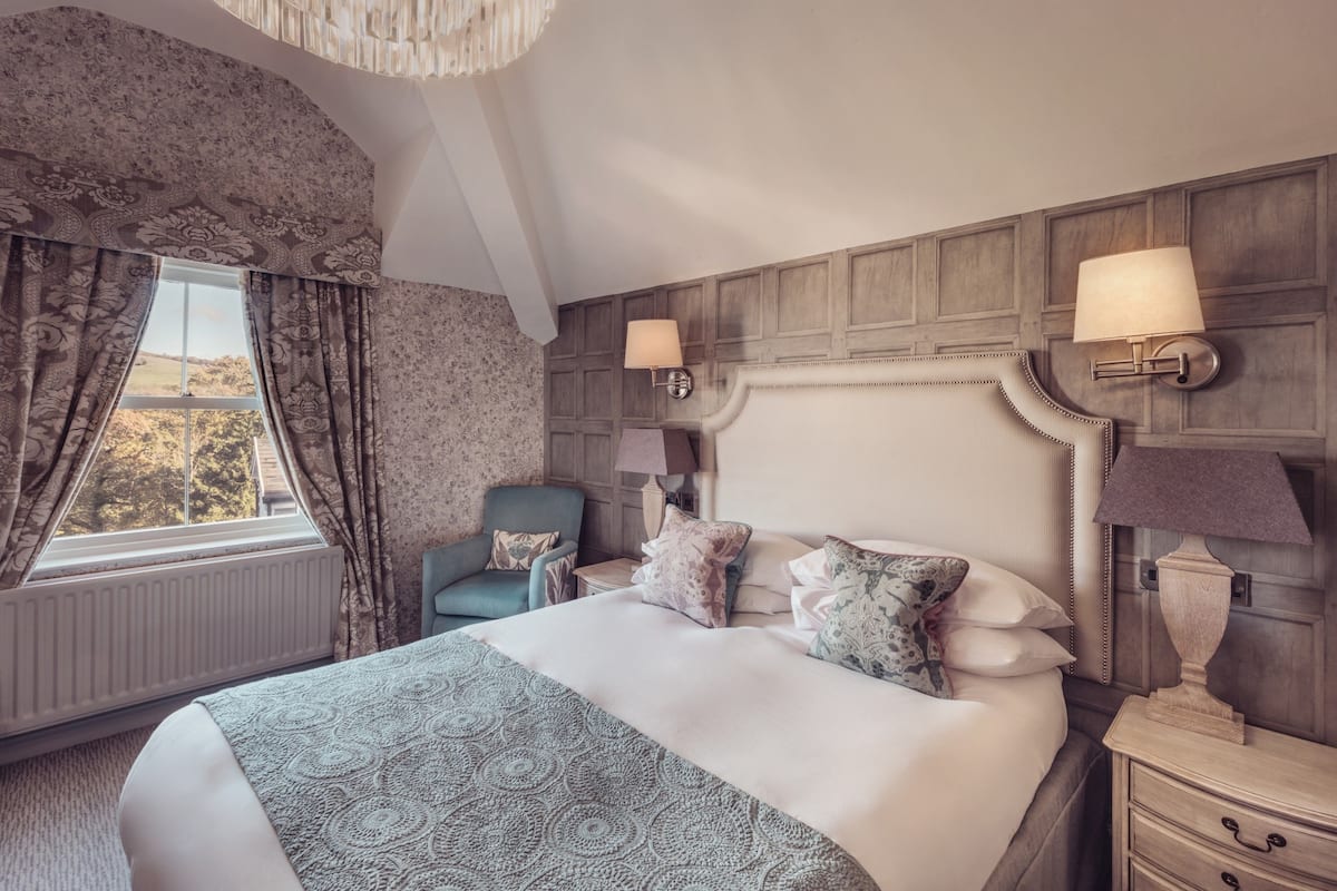 A bedroom with a large bed, two bedside lamps, a chair, and a view of the outdoors.