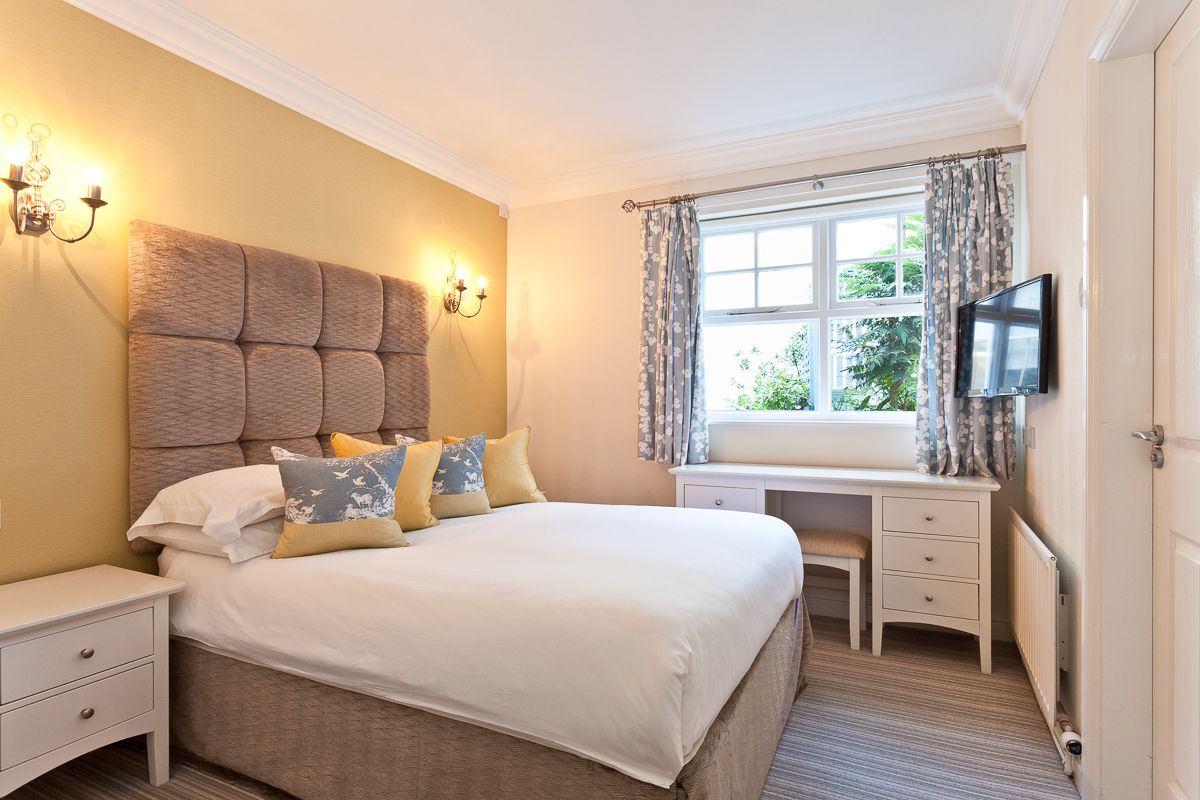 A bedroom with a large bed, bedside tables, a desk, and a TV.