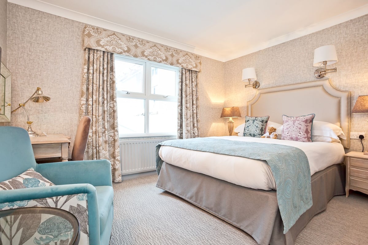 A bedroom with a large bed, a bedside table, a chair, and a window with curtains.