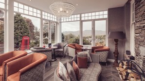 A cozy room with a large window, a chandelier, and a variety of seating options. - Windermere Hillthwaite Hotel (Windermere)