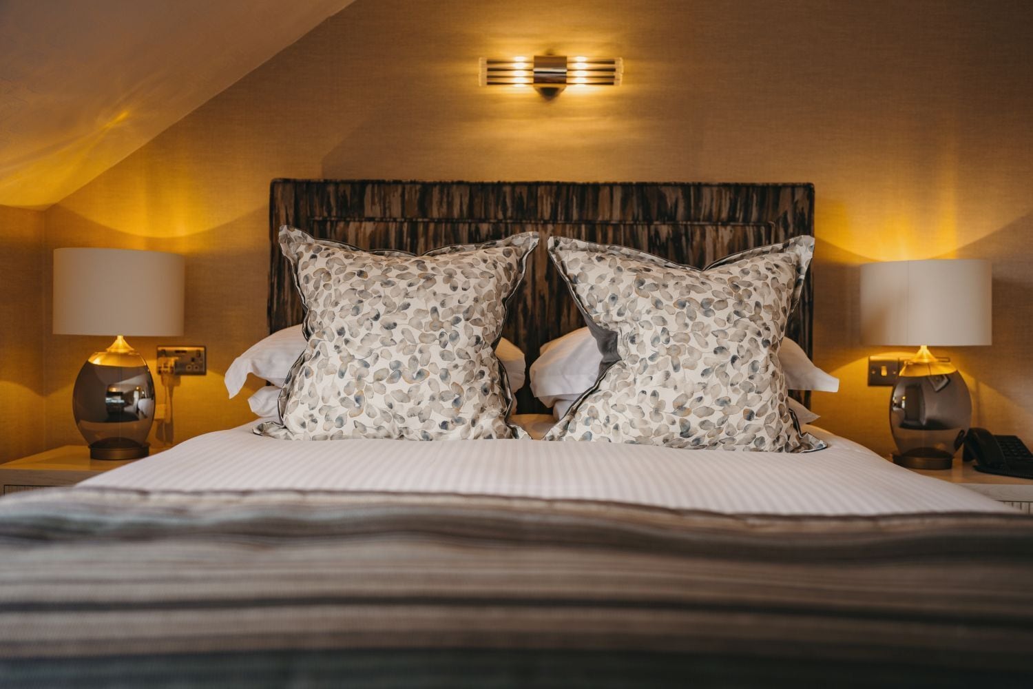 A hotel room with a large bed, two nightstands, and a wall-mounted light fixture.