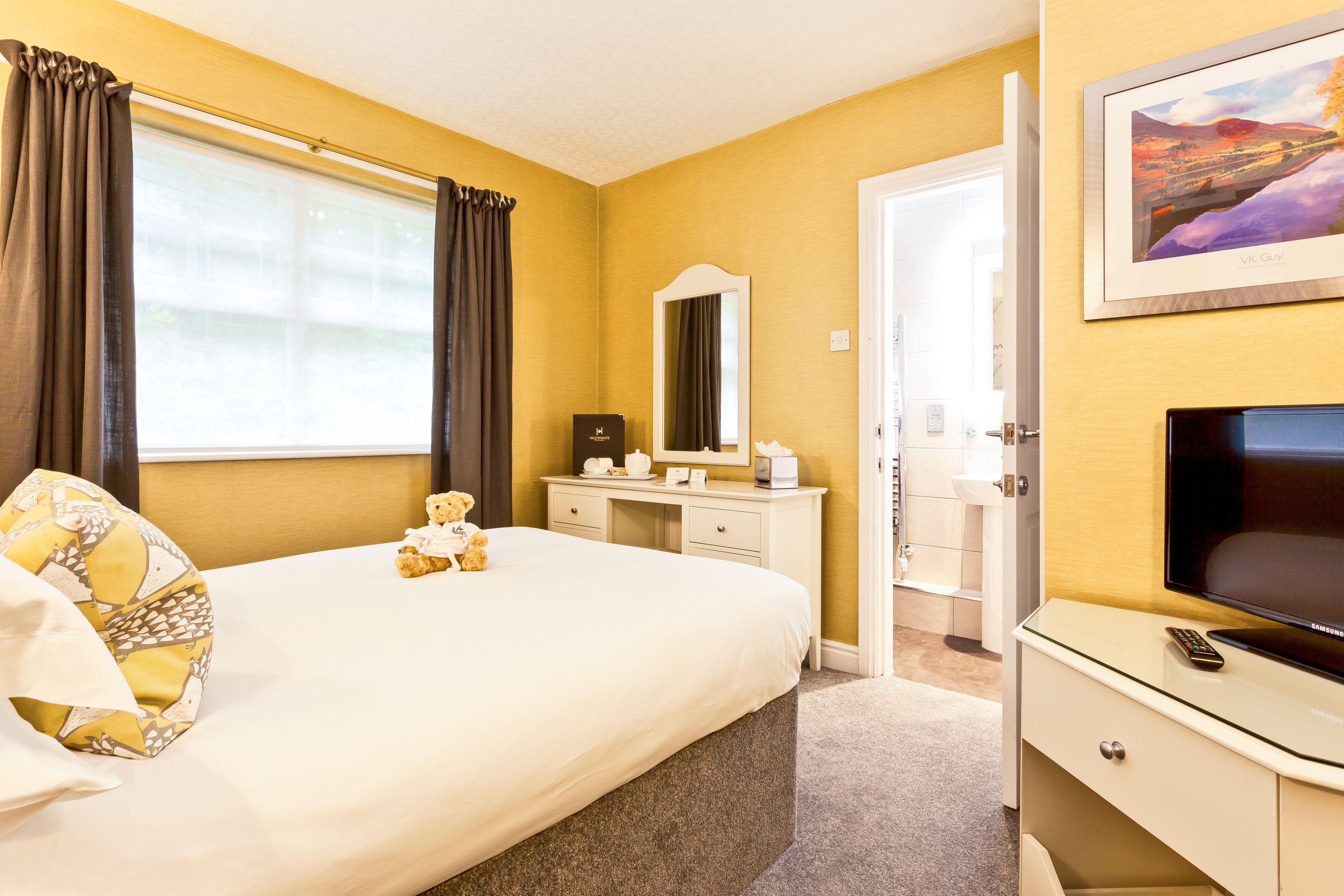 Habitación de hotel con una cama grande, una mesita de noche con control remoto, un aparador, un espejo y un cuadro en la pared.