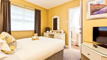Een hotelkamer met een groot bed, een nachtkastje met een afstandsbediening, een dressoir, een spiegel en een lijstje aan de muur.