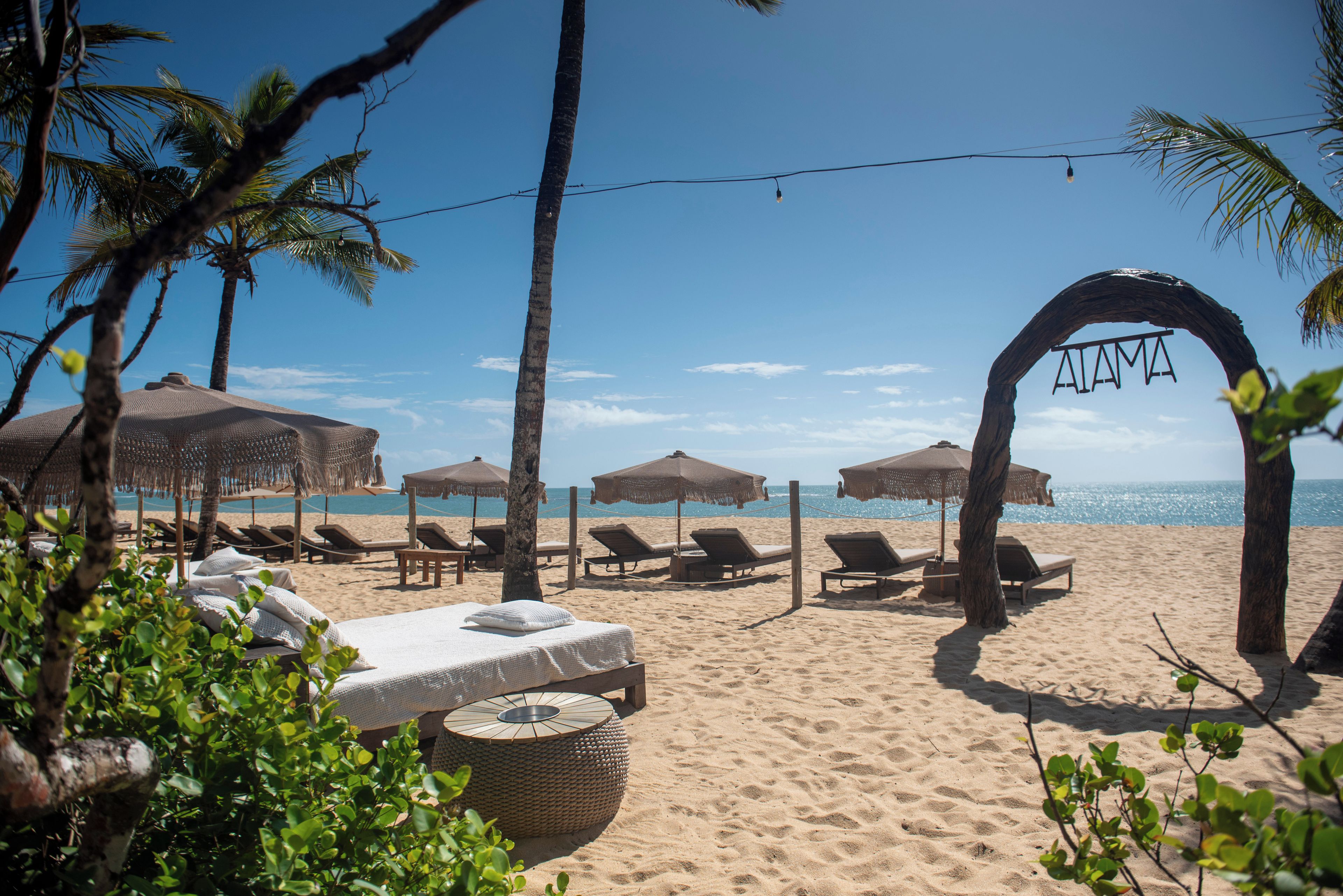 A beach with lounge chairs, umbrellas, and a decorative archway.