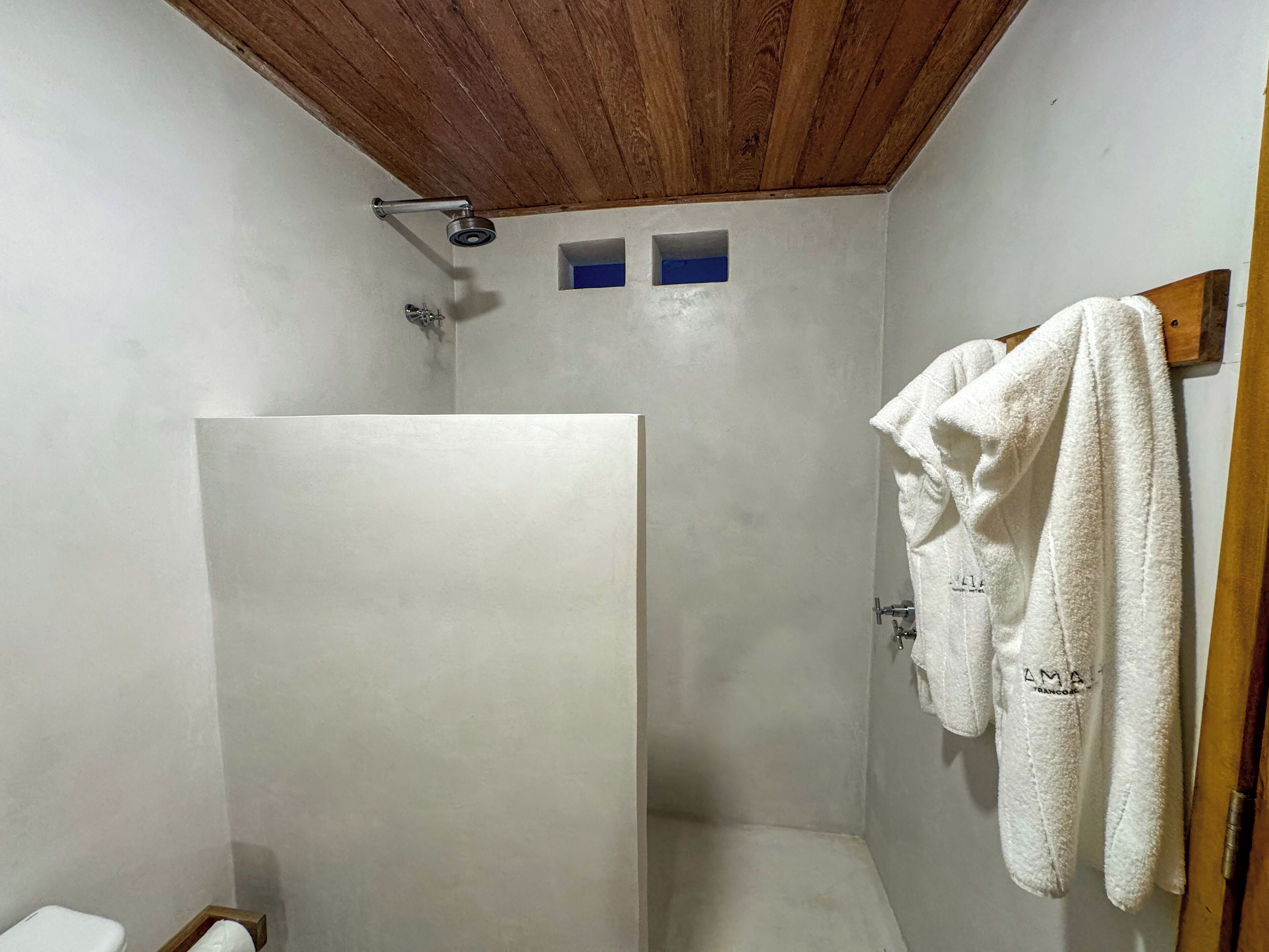Un espacio de ducha pequeño y cerrado, con techo de madera y una toalla blanca colgada en la pared.