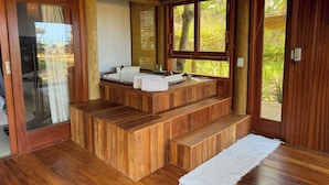 Un baño de madera con lavamanos integrado, una banca y un ventanal con vistas al verdor.