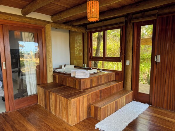 Une salle de bain en bois avec un lavabo intégré, un banc et une grande fenêtre donnant sur un paysage verdoyant.