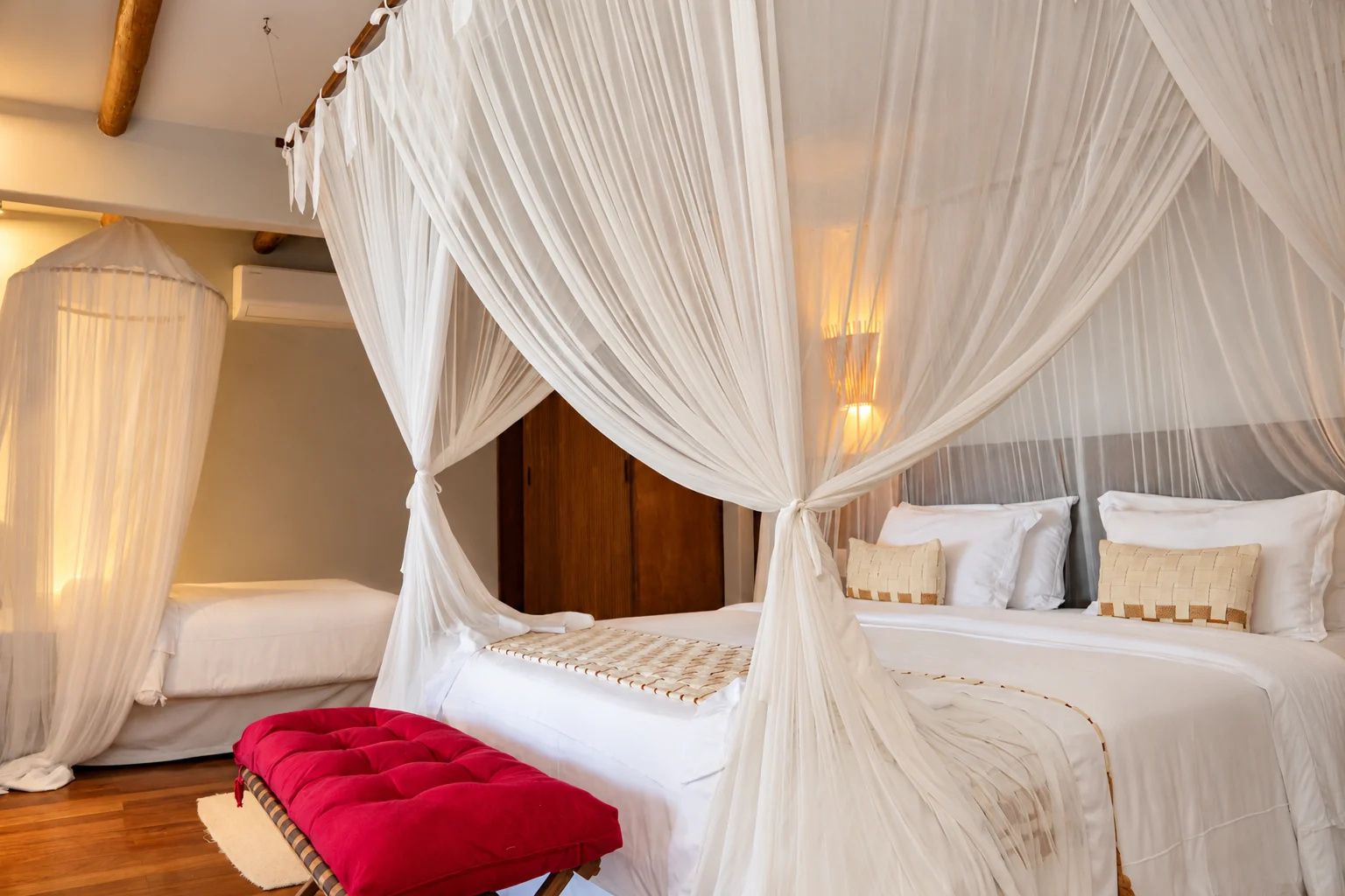 Un dormitorio con cama con dosel, un banco rojo y cabecera de madera.