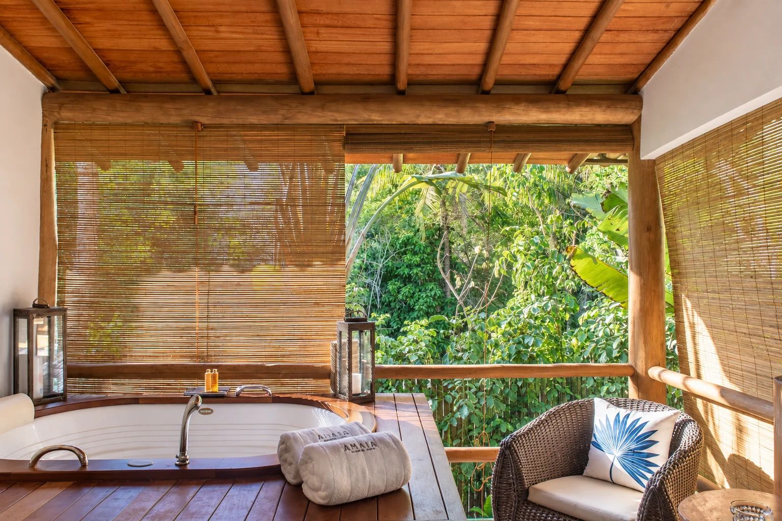 Um deck de madeira com banheira de hidromassagem, móveis de vime e cortinas de bambu.